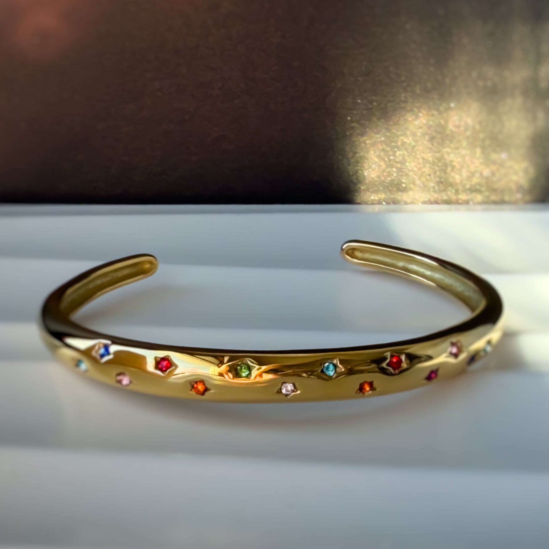 Close-up of Aerina rainbow bracelet showing colorful zircon stars on golden band.