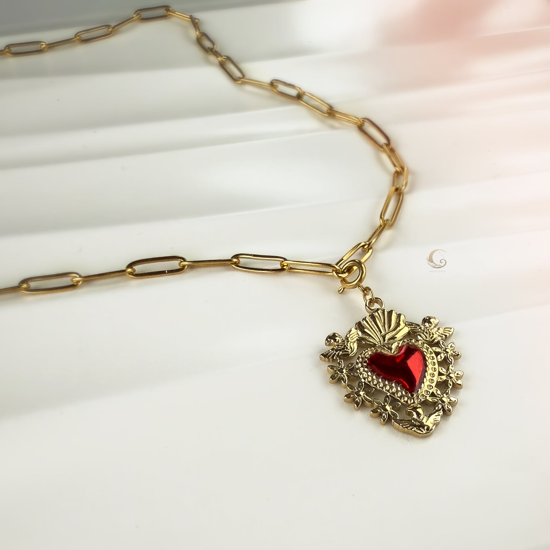 Close-up of Amara necklace featuring gold paperclip chain and ornate Sacred Heart red enamel pendant.