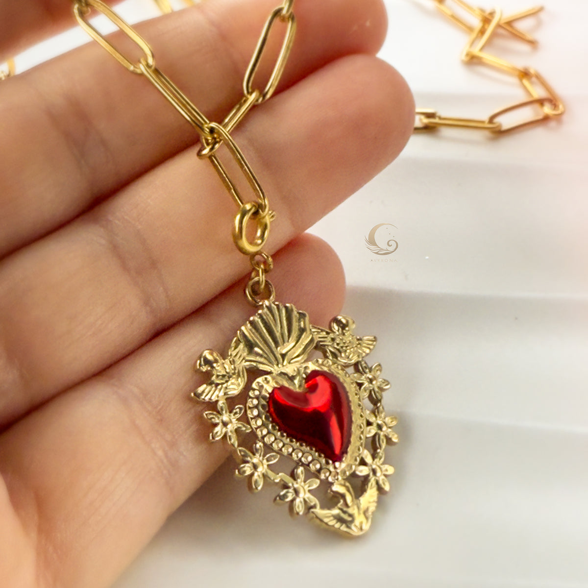 Hand holding the Amara Sacred Heart pendant, highlighting intricate golden frame and deep red enamel.