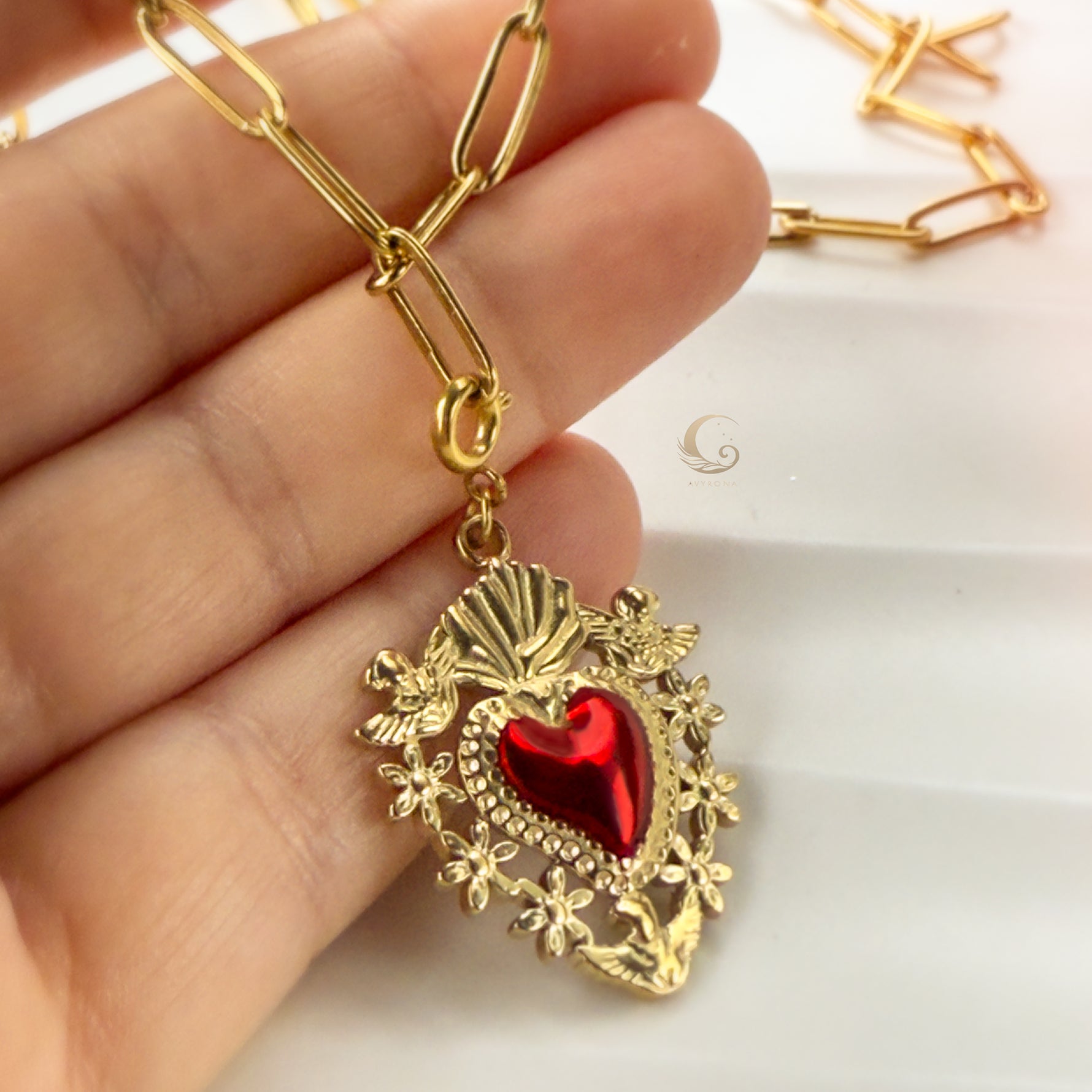 Hand holding the Amara Sacred Heart pendant, highlighting intricate golden frame and deep red enamel.
