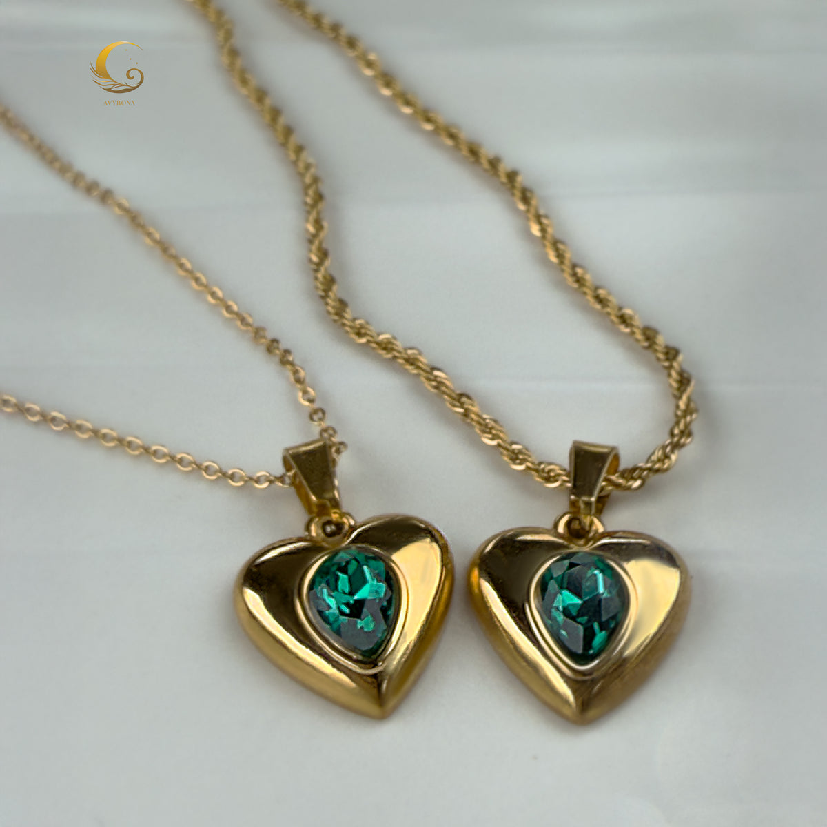 Twin green crystal heart necklaces laid side by side on white fabric