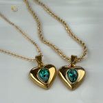 Twin green crystal heart necklaces laid side by side on white fabric