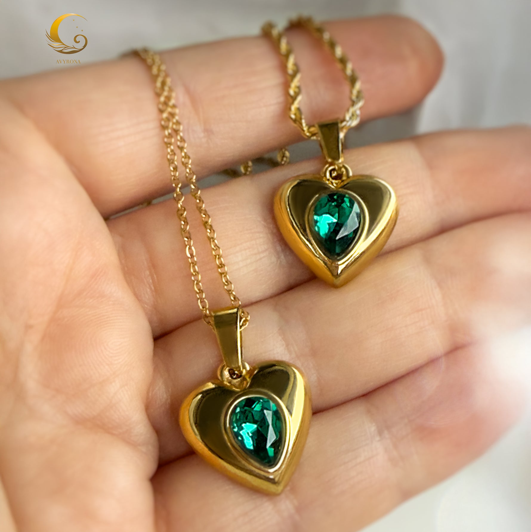 Two emerald green heart pendants shown in a hand, sparkling under natural light