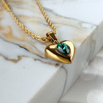 Single emerald heart charm pendant with twisted gold chain styled on marble background
