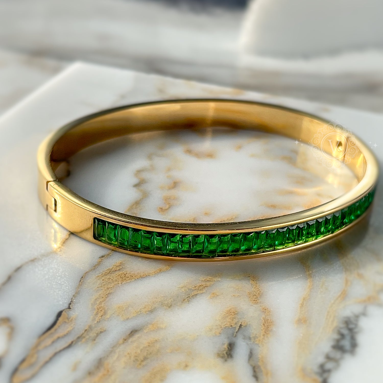 Full view of gold bangle bracelet with vibrant green crystals, placed on marble background – elegant and powerful look