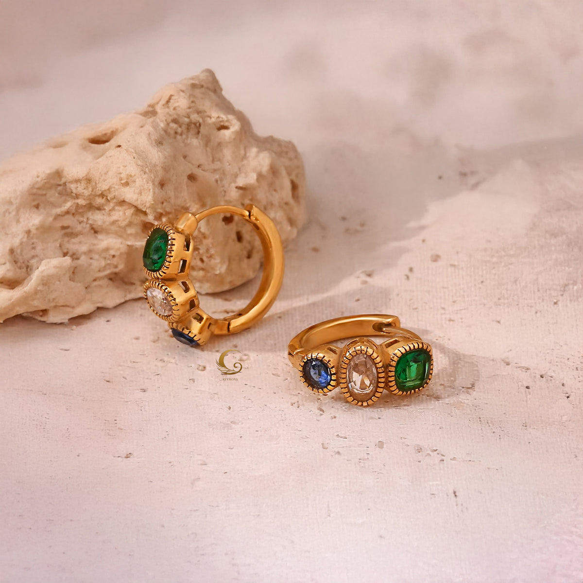 Aurora hoop earrings with three zircon stones placed next to textured beige rock