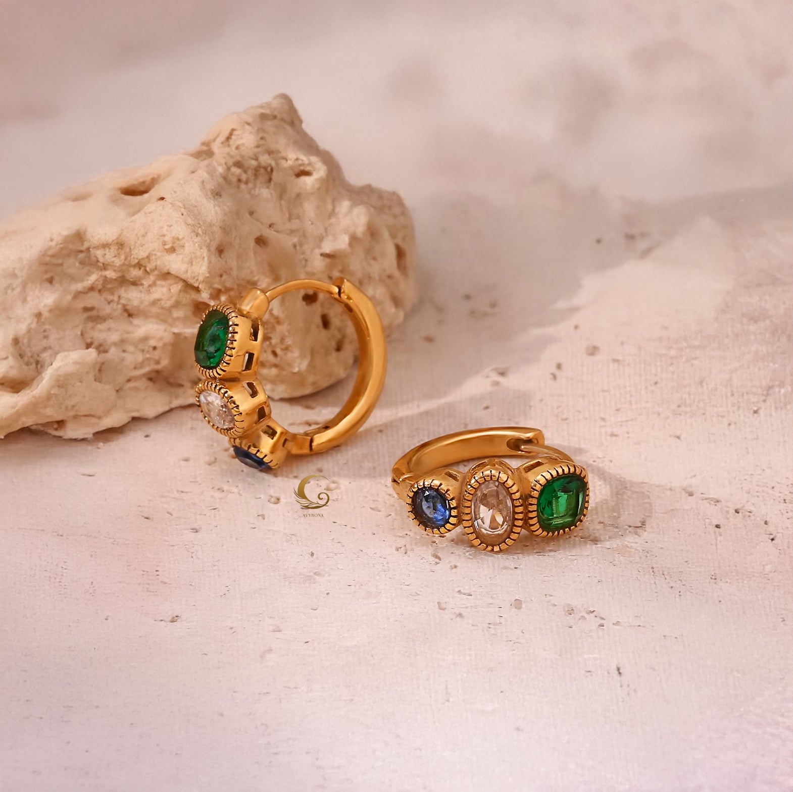 Aurora hoop earrings with three zircon stones placed next to textured beige rock