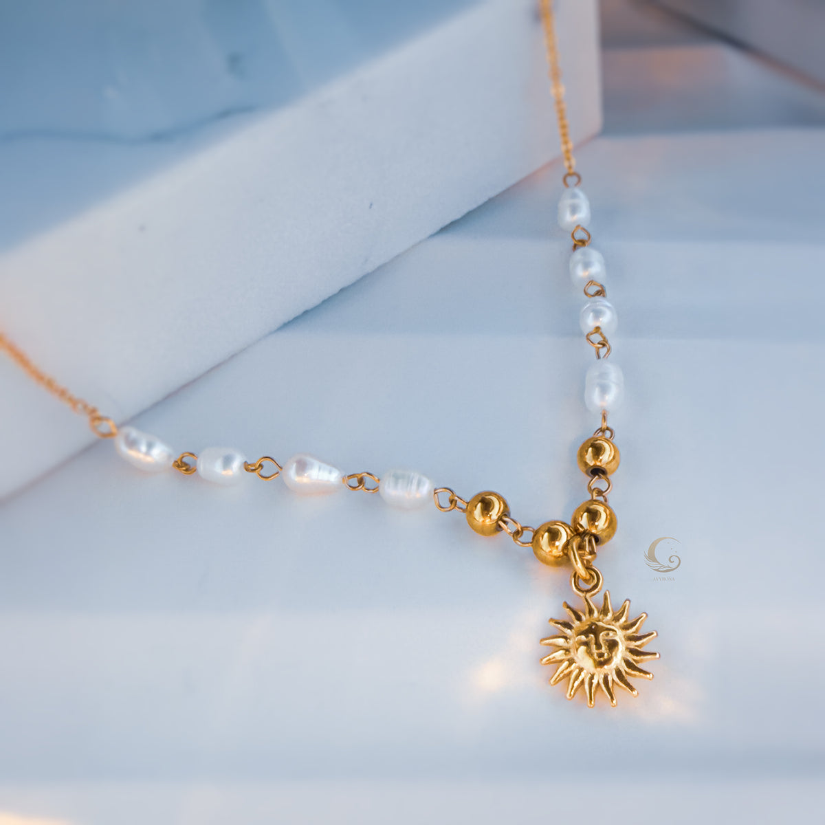 Close-up of gold and pearl beaded necklace with a sun pendant, displayed on marble surface.