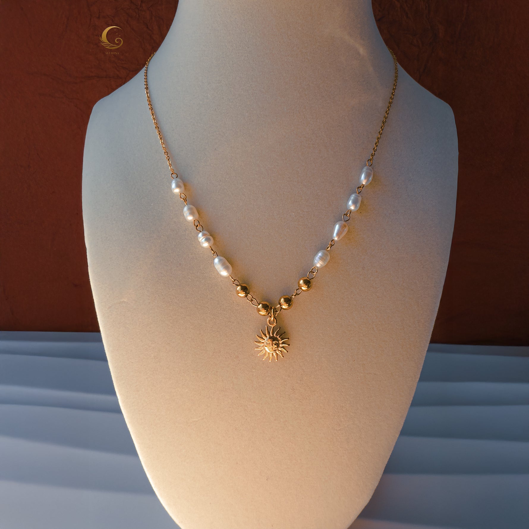 Ayla necklace displayed on bust, featuring white pearls, gold beads, and radiant sun pendant.