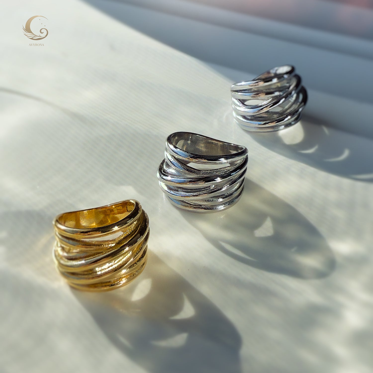 Close-up of the gold and silver Branch Rings lying on a light surface, showing their flowing, nature-inspired sculptural design.