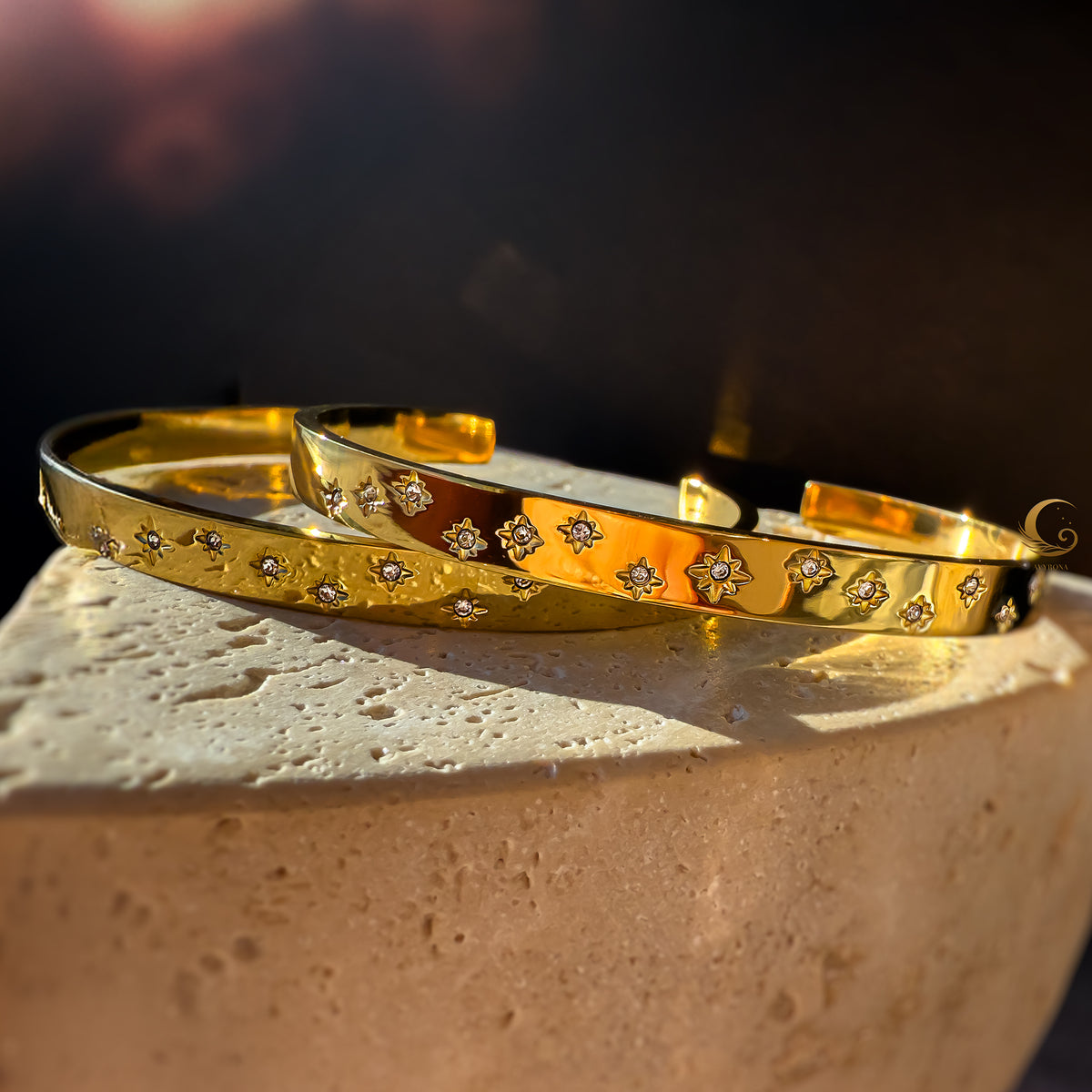 Gold stainless steel cuff bracelet with engraved stars, presented on a marble surface with soft reflections.