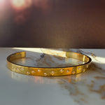 Minimalist gold bracelet styled with others in a layered stack on the wrist, showing variation of celestial designs.