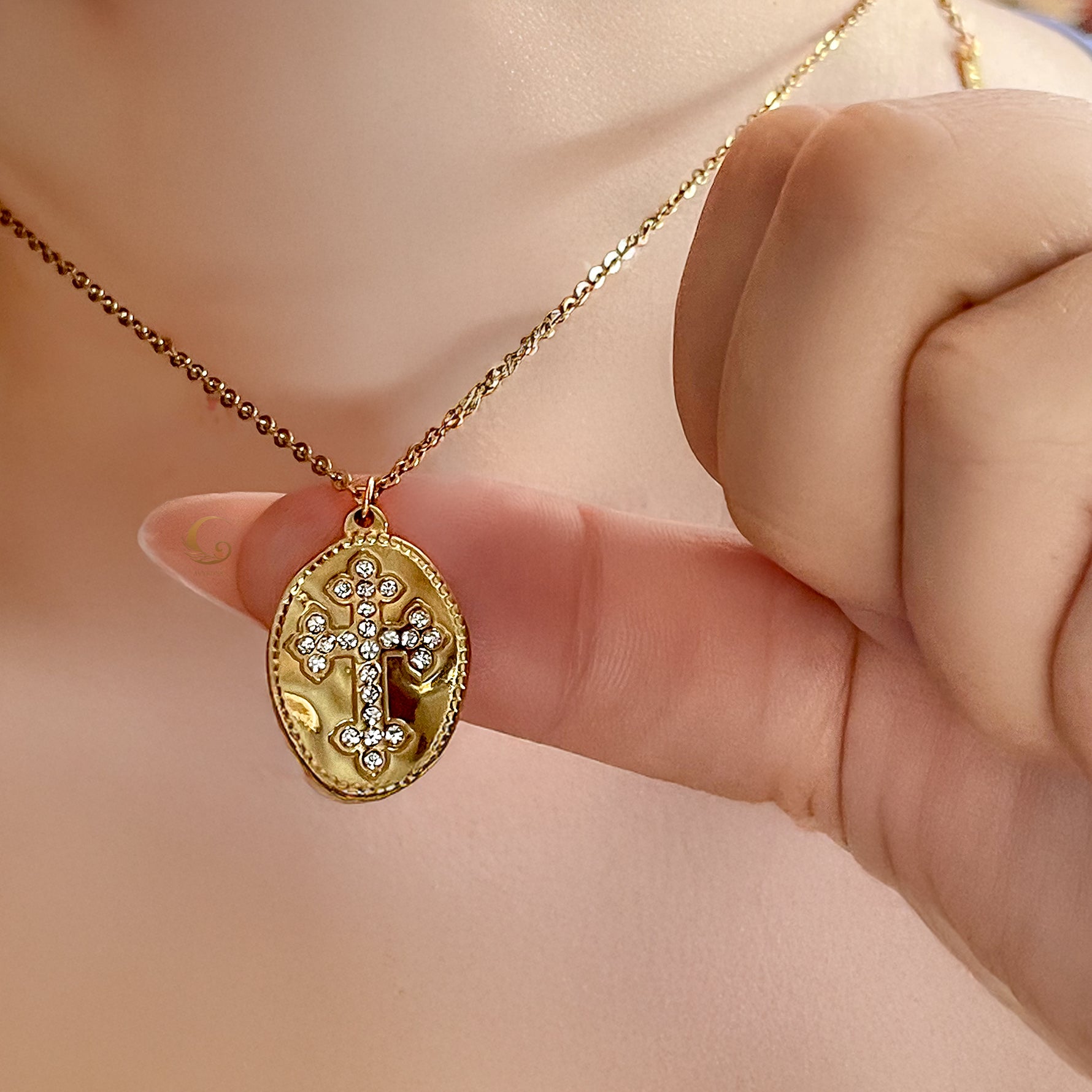 Celestia gold cross necklace gently held between fingers to show pendant size and sparkle against skin.
