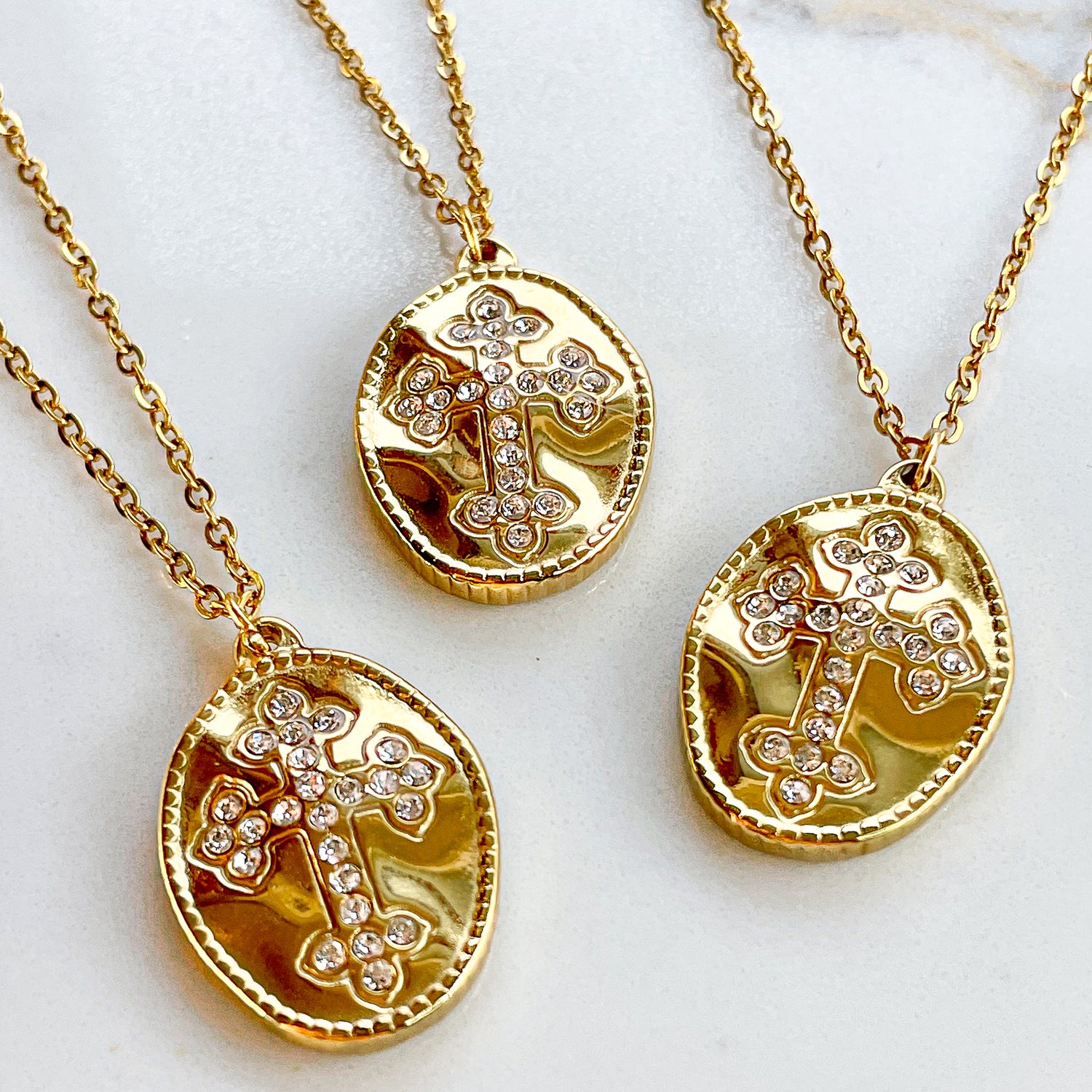 Three gold-plated cross medallion necklaces lying on a soft fabric, highlighting their sparkling cubic zirconia details.