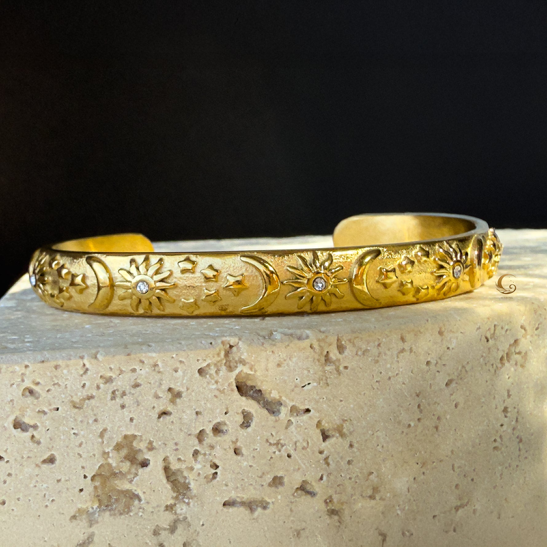 Full front view of the celestial cuff bracelet placed on stone, highlighting the matte 18K gold finish and engraved cosmic patterns with zircon sparkle.