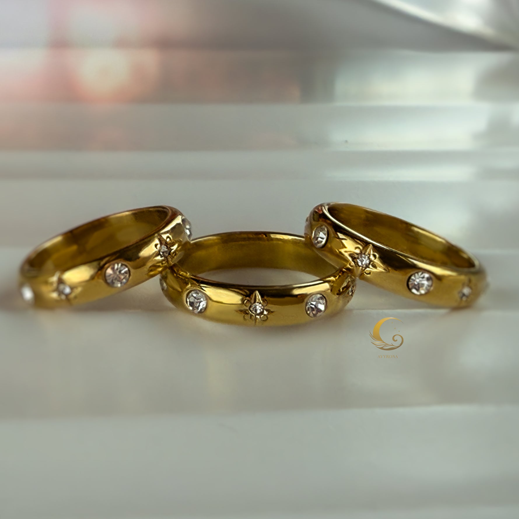 Trio of Celestial Glow rings with crystal and star details on soft white surface