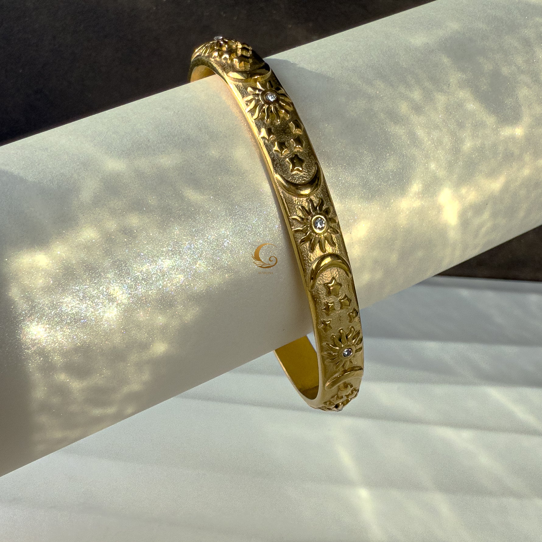 Diagonal close-up of the celestial bracelet resting on an elegant rolled surface, capturing symbolic engravings and gold polish.
