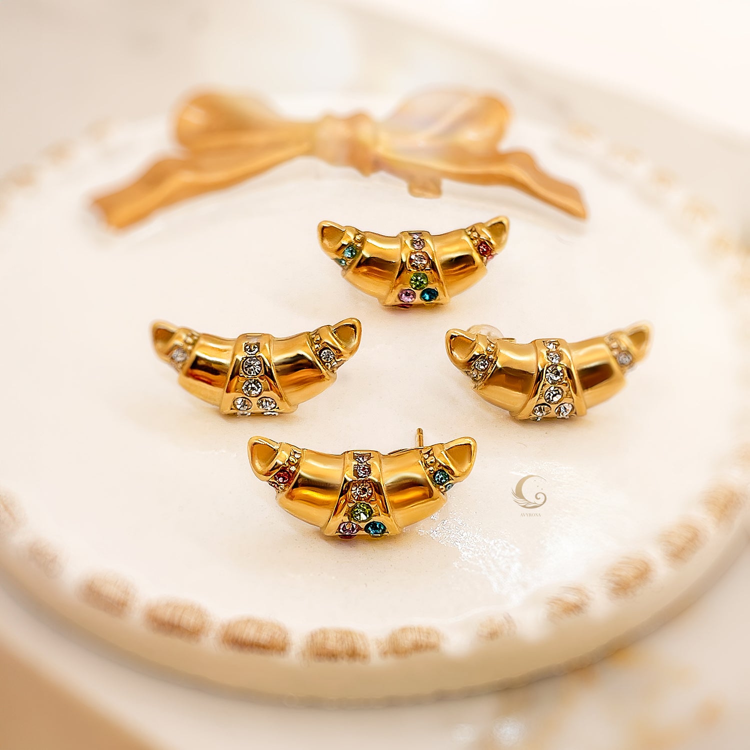  Close-up of four gold croissant-shaped earrings with cubic zirconia on a soft white surface