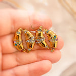  Hand holding four gold croissant-shaped earrings in clear and multicolored versions