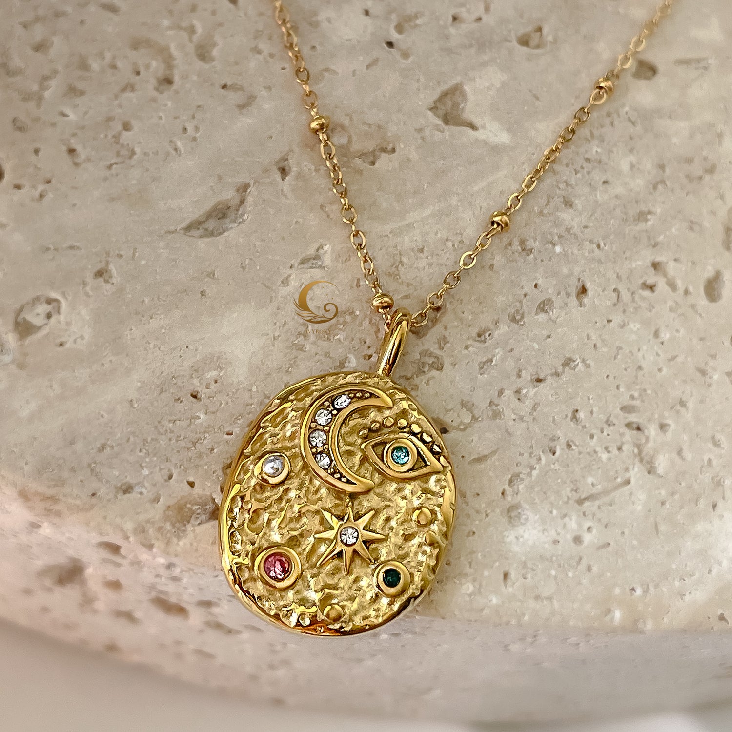 Close-up of gold medallion necklace with celestial moon, star, and Evil Eye symbols on textured stone background