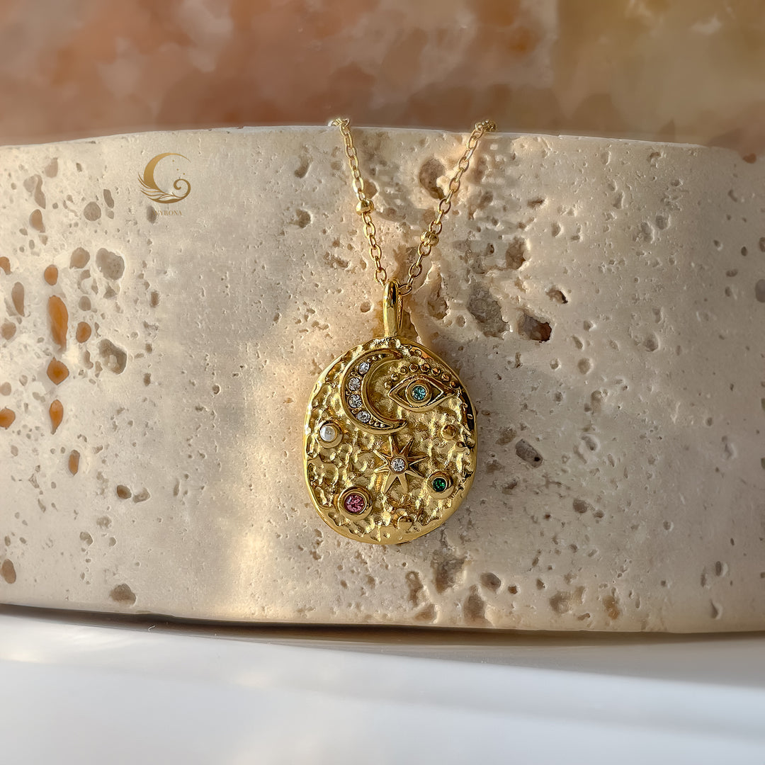 Celestial medallion necklace displayed flat on warm stone surface, showing engraved moon and star details