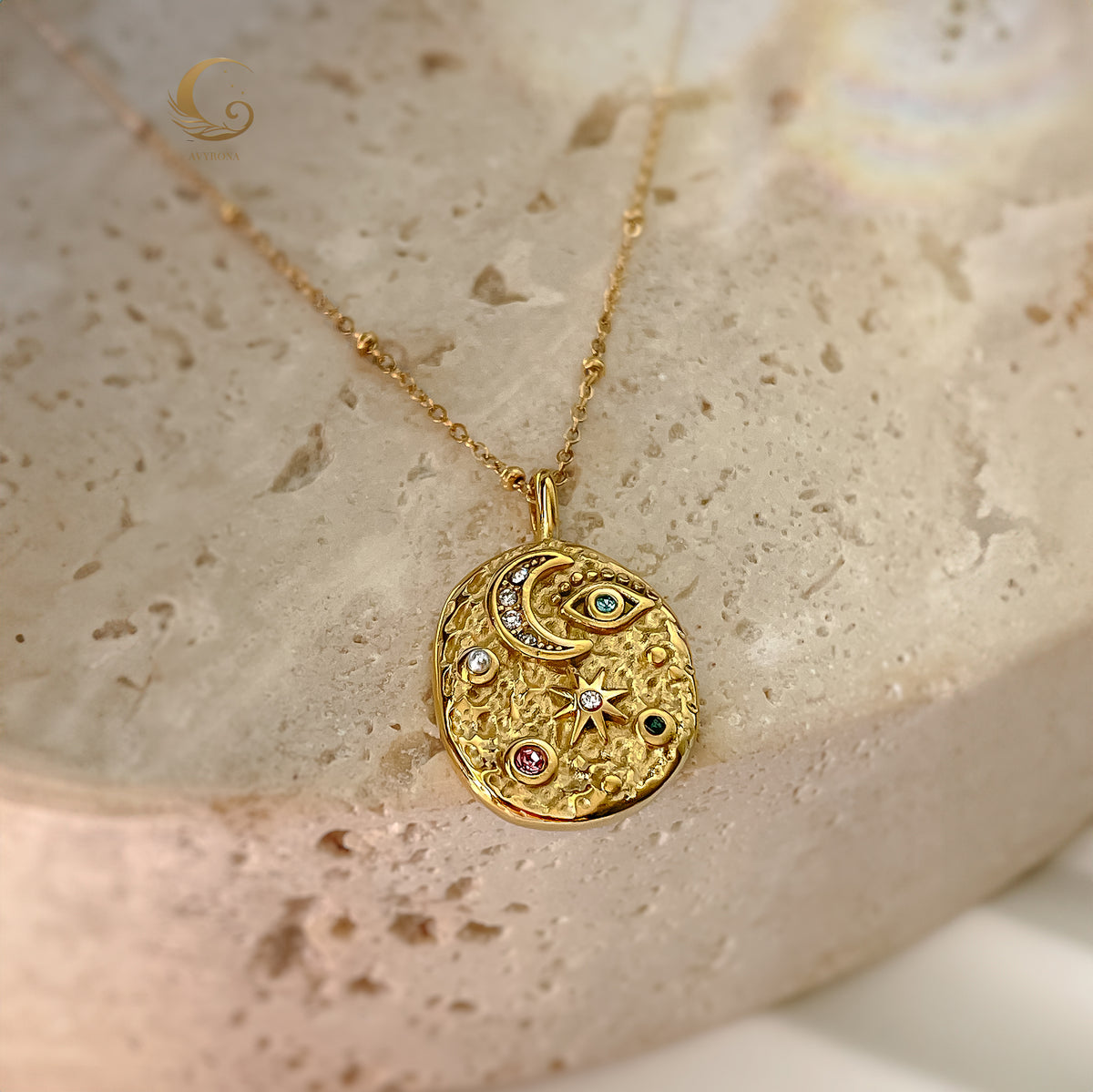 Gold-plated celestial pendant necklace with multicolor crystals, styled on creamy textured background