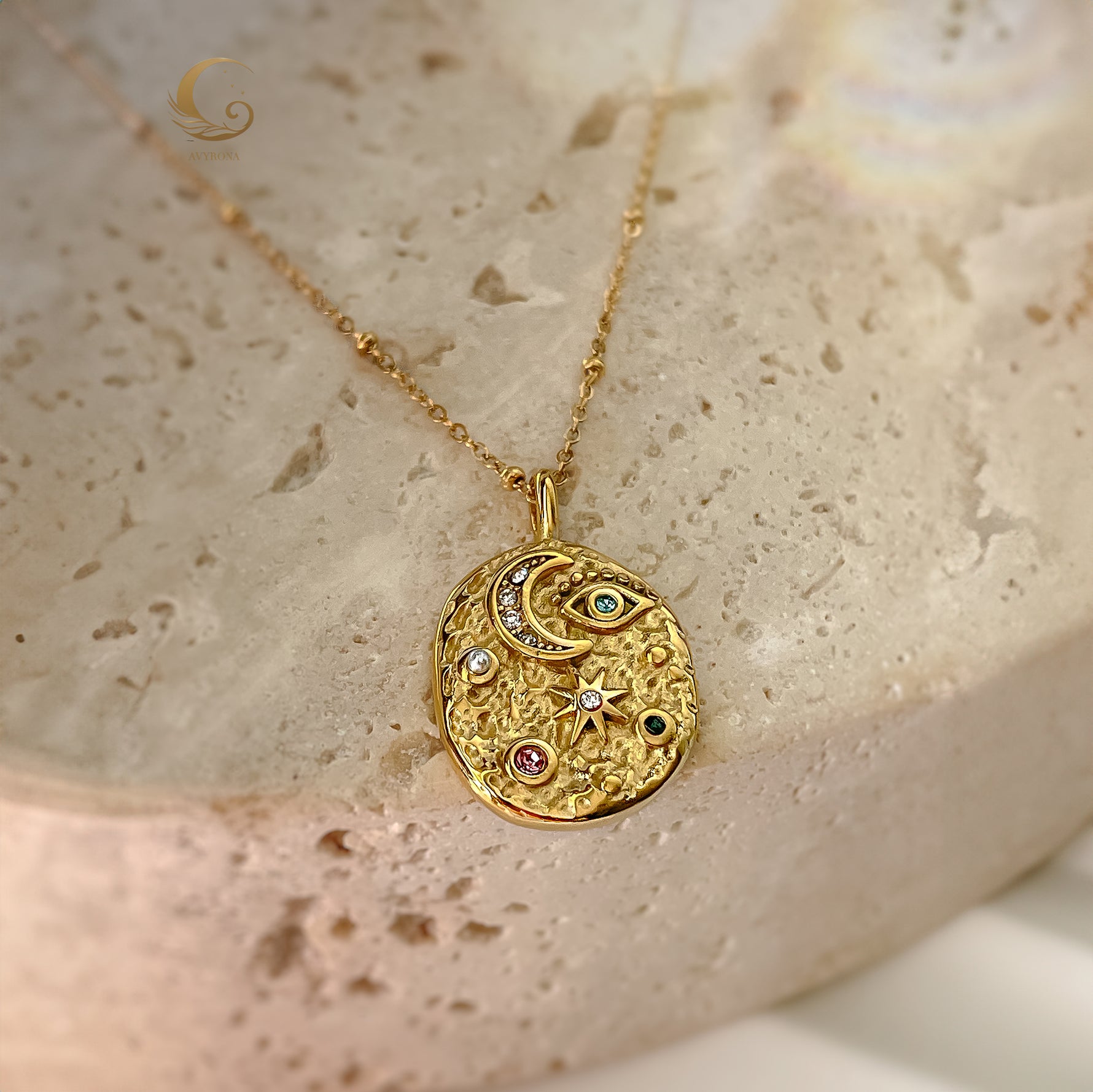Gold-plated celestial pendant necklace with multicolor crystals, styled on creamy textured background