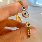 Close-up of gold bangle bracelet with Evil Eye symbol and blue crystals, held in hand