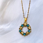 Single Elina necklace photographed against a silky white fabric. The round pendant features alternating hearts and light blue crystals in a full circle.