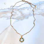 Full view of the Elina necklace laid flat on marble surface. The pendant hangs from a delicate gold chain with a clasp and extender visible at the top.
