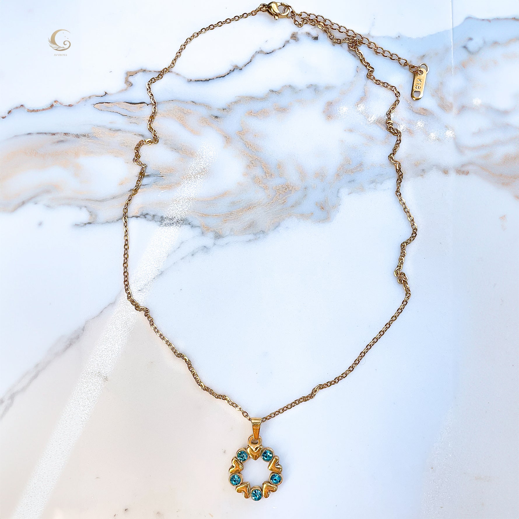 Full view of the Elina necklace laid flat on marble surface. The pendant hangs from a delicate gold chain with a clasp and extender visible at the top.