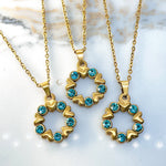 Three Elina necklaces displayed on a marble background. Each pendant shows heart-shaped gold accents paired with bright blue crystals forming a wreath.