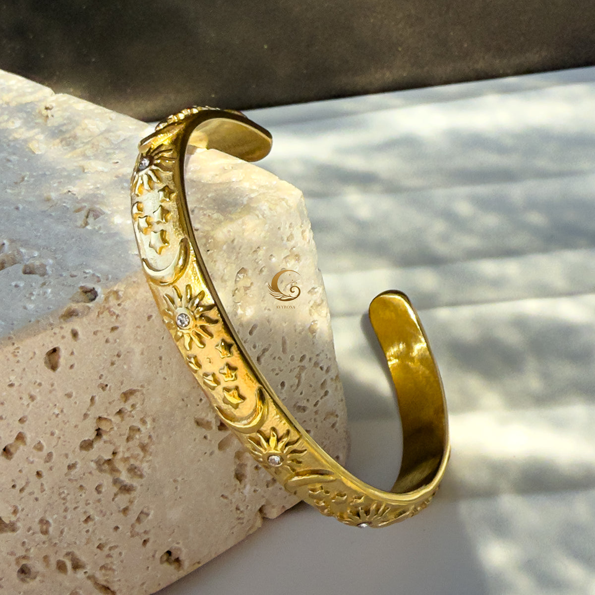 Artistic angled shot of the open cuff bracelet showing depth of celestial engravings and shimmering cubic zirconia, photographed on warm marble.