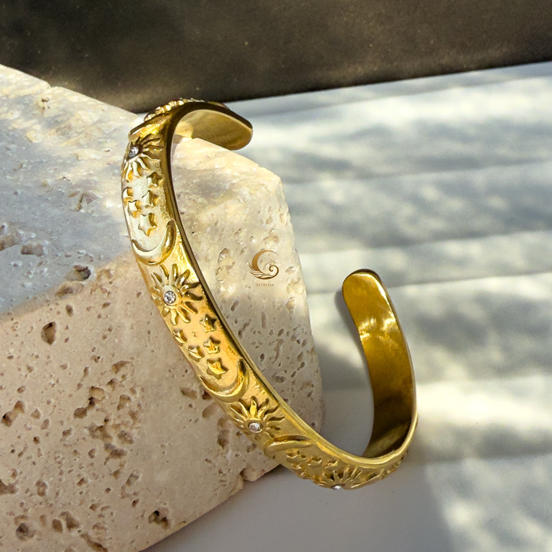 Artistic angled shot of the open cuff bracelet showing depth of celestial engravings and shimmering cubic zirconia, photographed on warm marble.