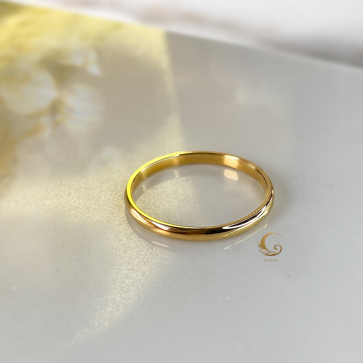 Close-up of single 2mm gold band ring on marble background with Avirona logo.