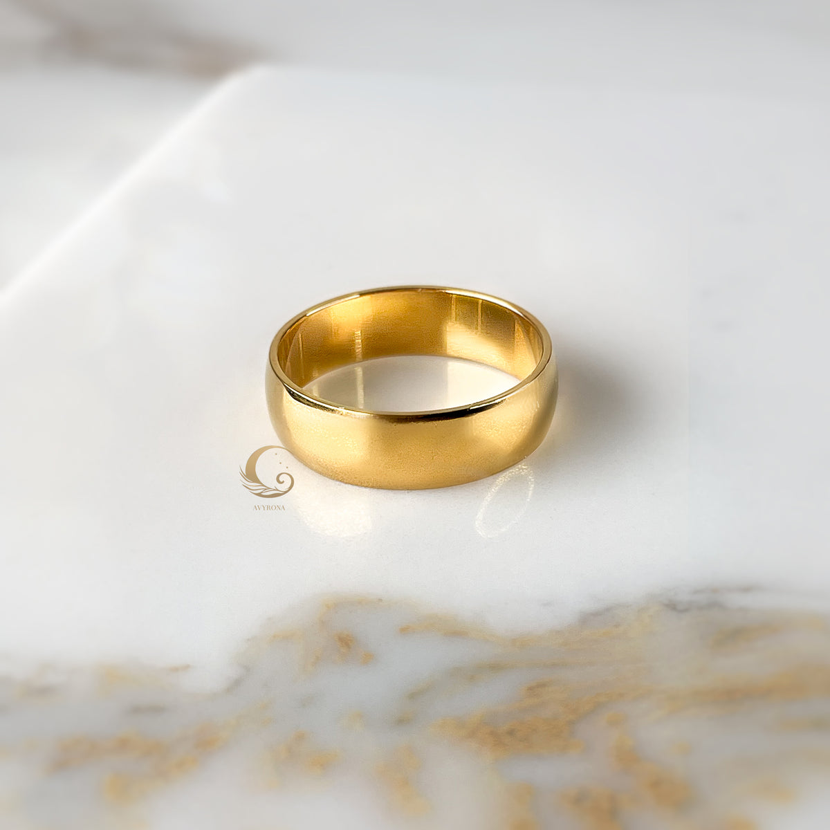 6mm gold ring band laid flat on white and gold marble.