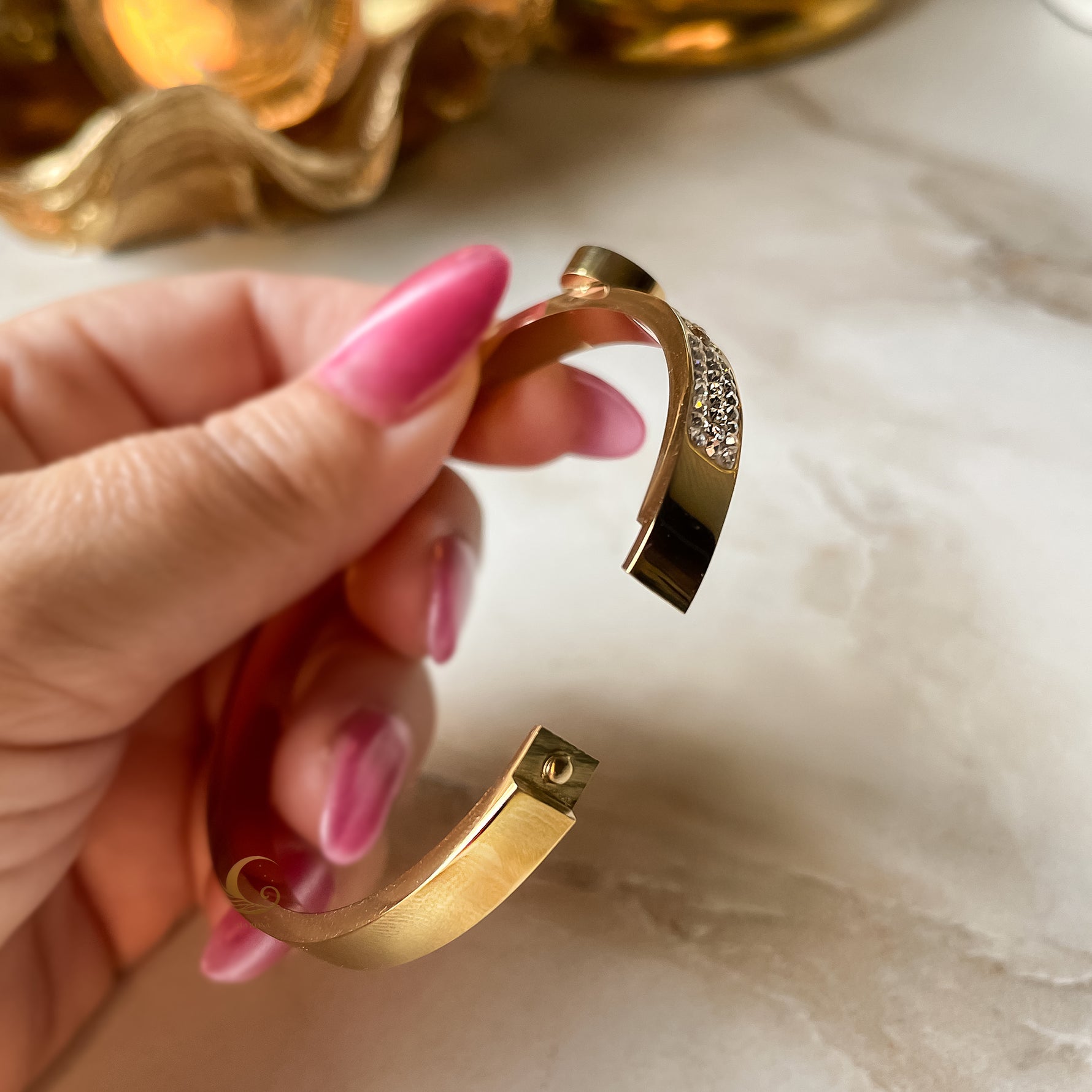 Open bangle bracelet with side clasp, showing inside structure and smooth gold finish.