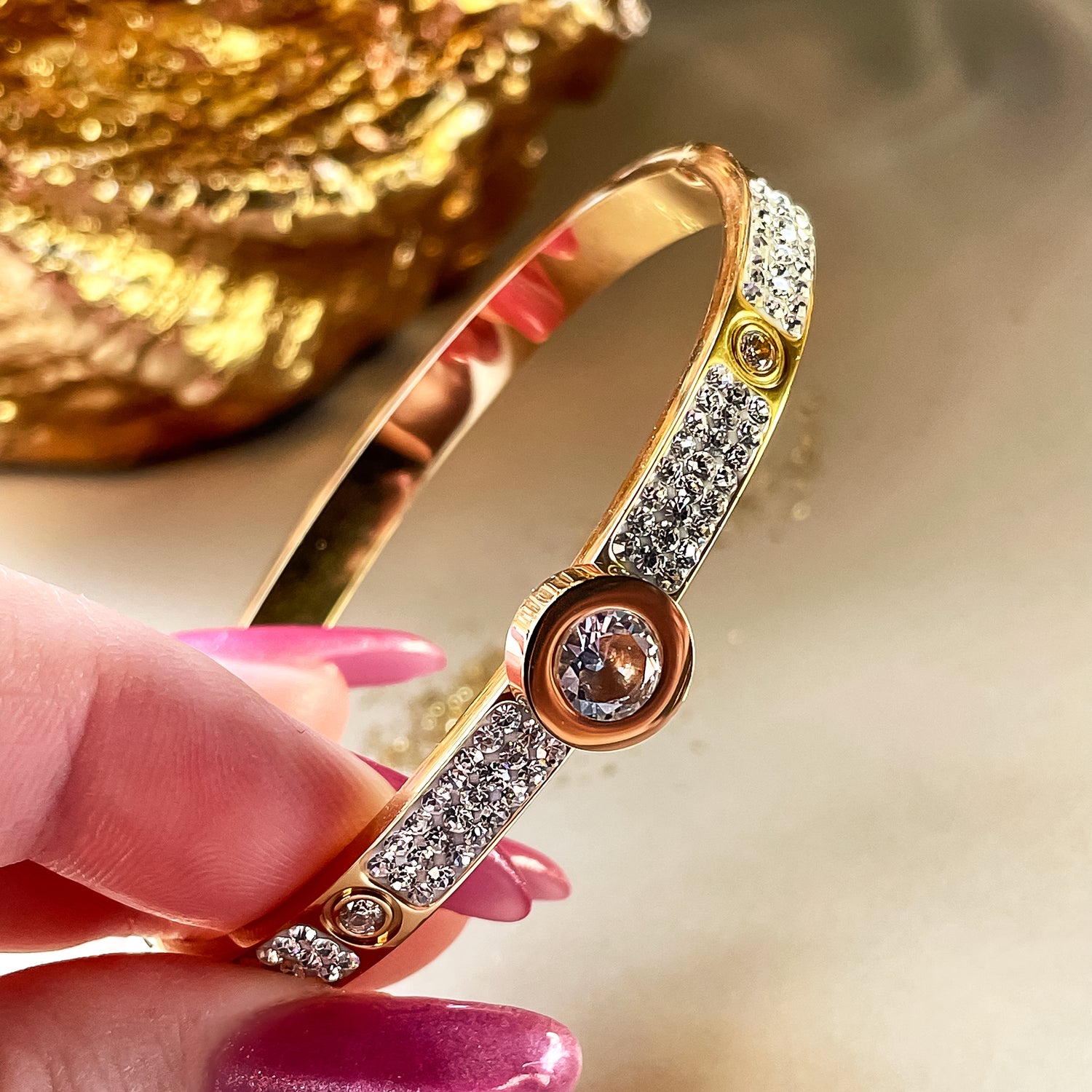 Elegant bangle bracelet held in hand, showing sparkling zirconia crystals under golden light reflections.