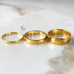Three gold bands aligned side by side in increasing width order on bright stone surface.