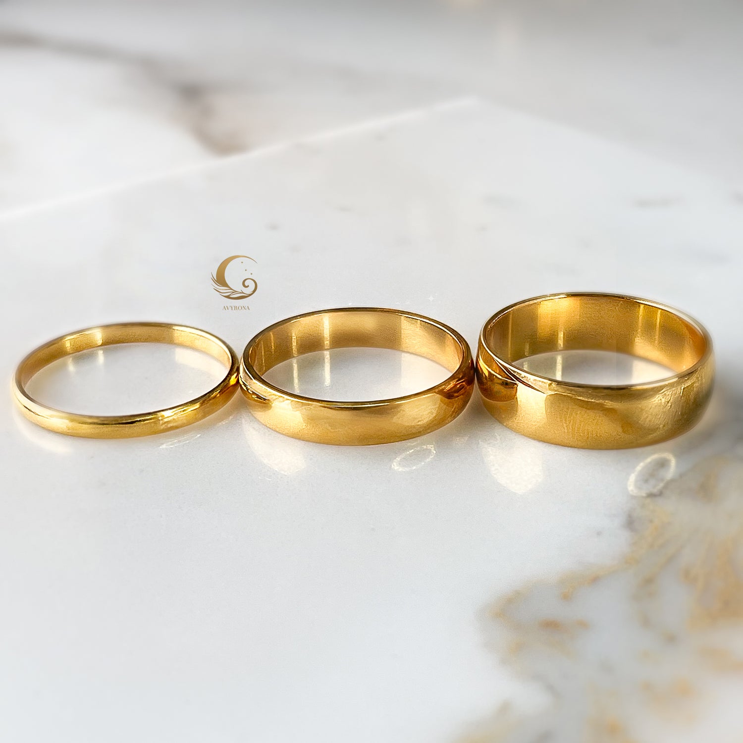 Three gold bands aligned side by side in increasing width order on bright stone surface.