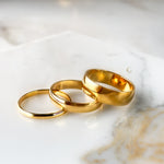 Set of three gold ring bands in different widths (2mm, 4mm, 6mm) displayed on marble.
