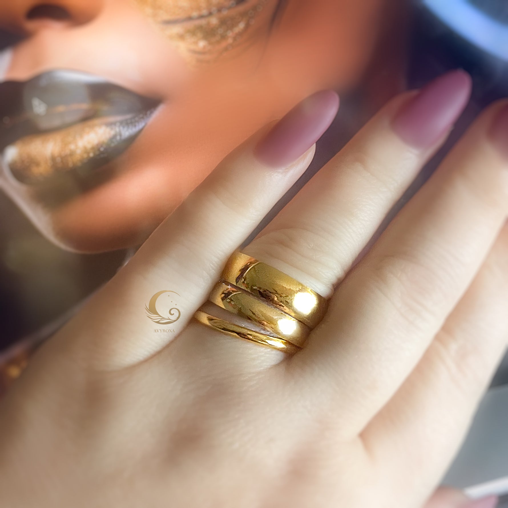 Hand wearing three stacked gold rings of different widths, styled with warm-toned makeup.