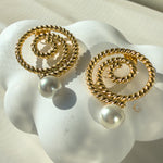 Close-up of Thaleia gold spiral earrings with pearl-like beads on a soft white seashell