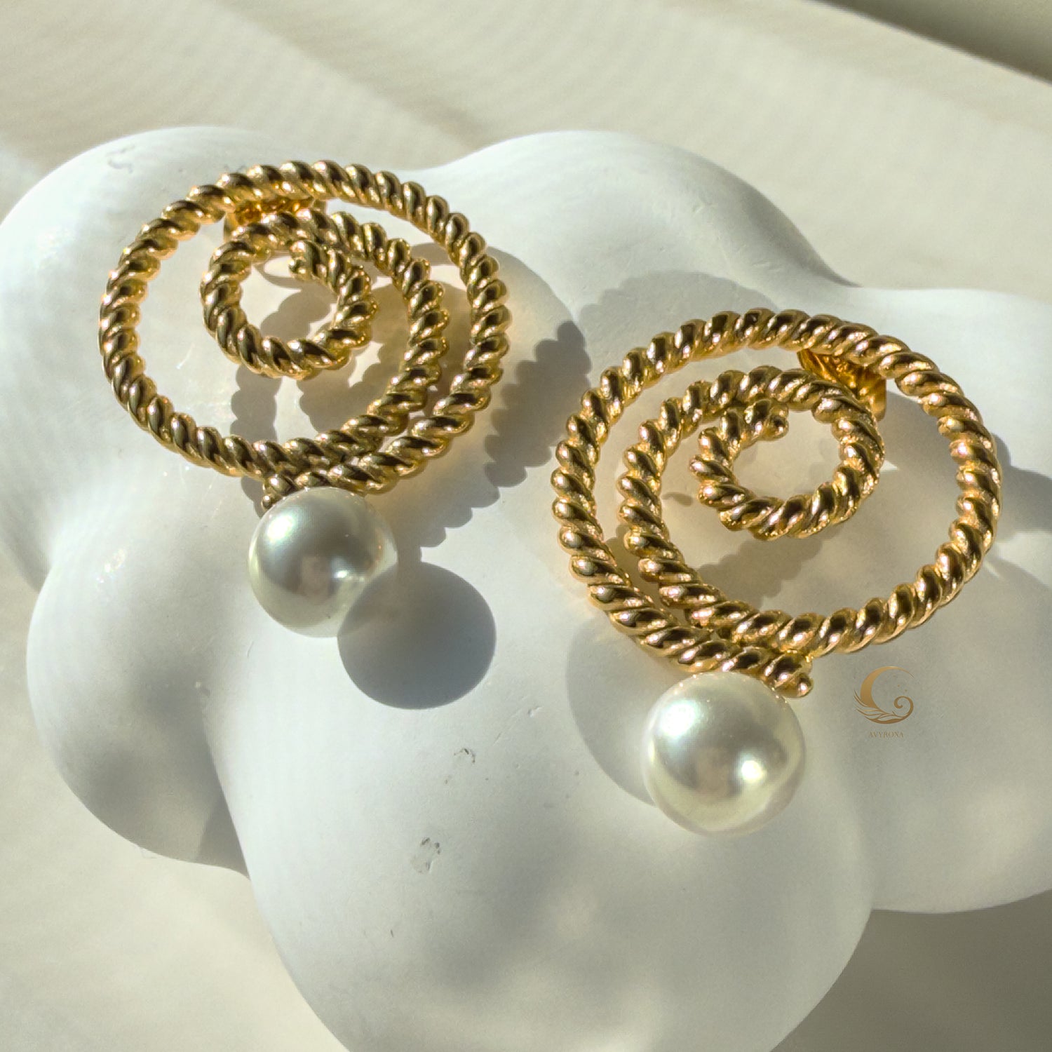 Close-up of Thaleia gold spiral earrings with pearl-like beads on a soft white seashell
