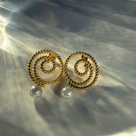 Gold Thaleia earrings with twisted spirals and pearl-like drops, shining in soft light