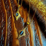 Two Guardian Eye necklaces with black cat eye stones on gold chains, shown on a dark wooden textured background with golden accents.