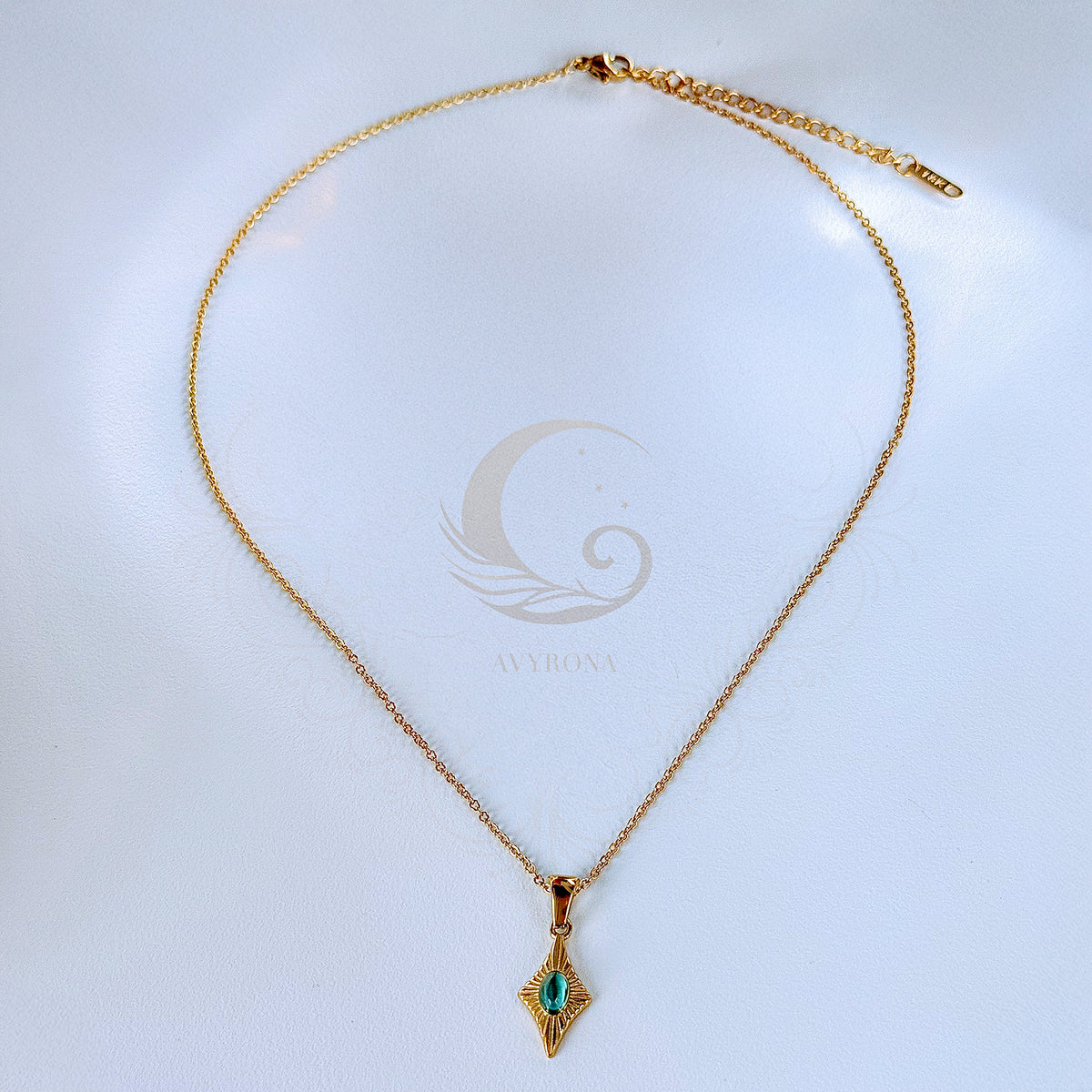 Full view of Guardian Eye necklace with blue cat eye stone pendant on a gold chain with extender, laid flat on Avyrona branded background.