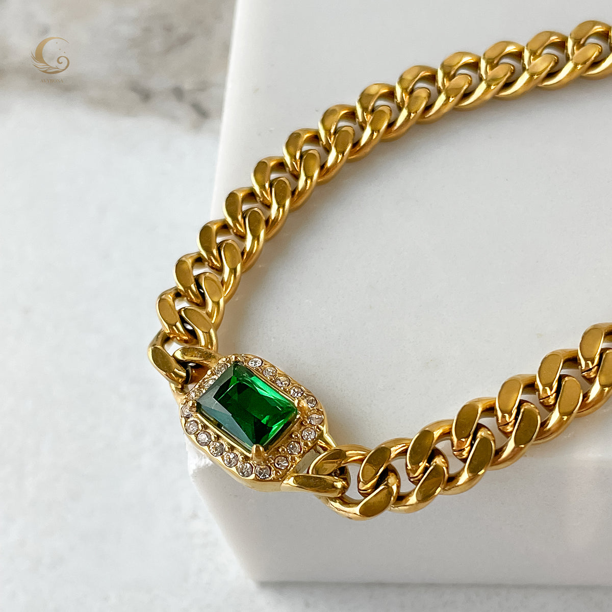 Close-up of Harper Bracelet with green crystal and sparkling zirconia on thick cuban chain, displayed on soft white surface.