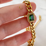 Harper Bracelet held between fingers, highlighting deep green crystal and chunky gold chain detail.