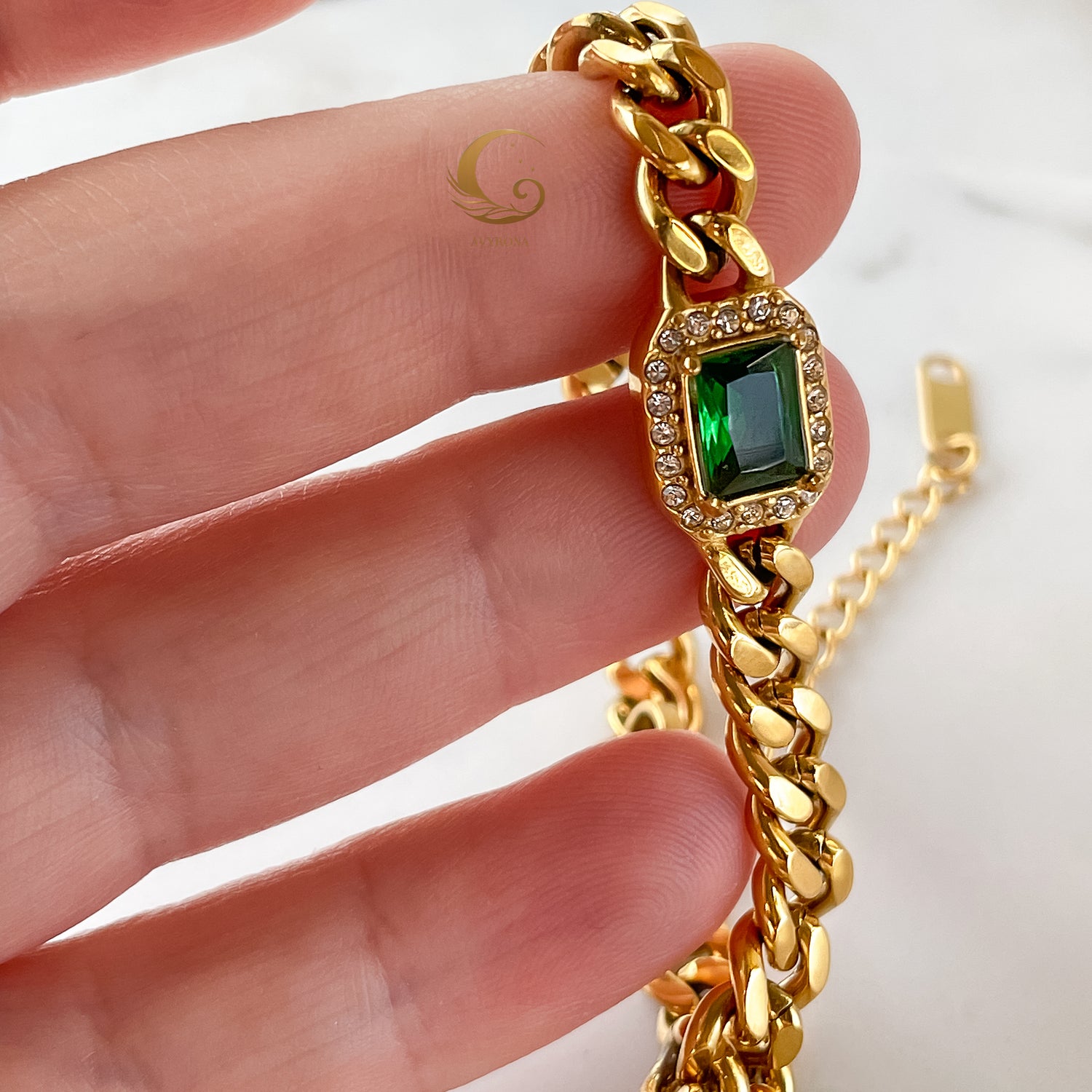 Harper Bracelet held between fingers, highlighting deep green crystal and chunky gold chain detail.